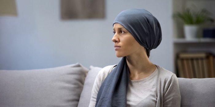 upset young lady in headscarf lonely sitting on sofa in oncologic hospital