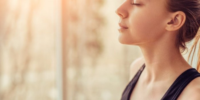 side view of young female with closed eyes breathing deeply while doing respiration exercise during yoga session in gym