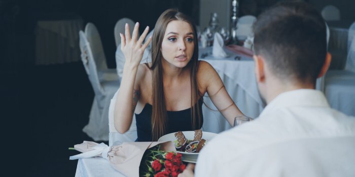 angry young woman is quarreling with her lover while dining in restaurant, shouting and gesturing emotionally bouquet of ...