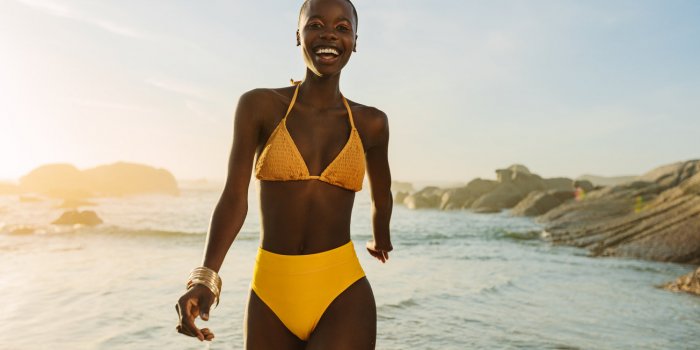 attractive african woman in yellow bikini walking along the beach smiling female in swimwear coming out of the sea water ...