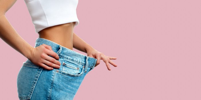 diet concept and weight loss woman in oversize jeans on pastel pink background