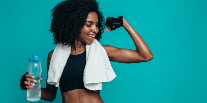 young fitness woman flexing muscles and smiling against blue background african female model in sportswear showing her mu...
