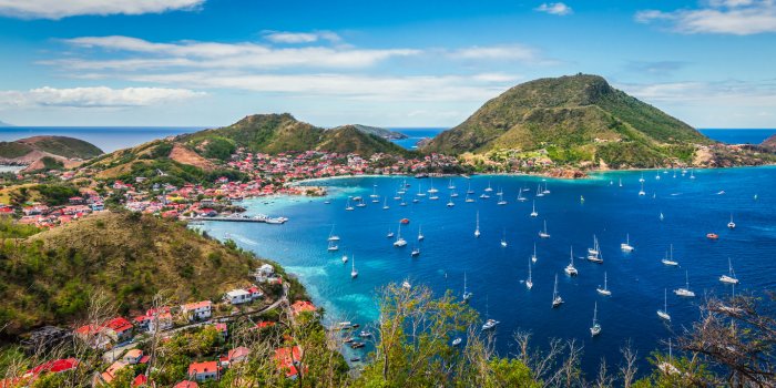 colorful image of guadeloupe terre de haut bay and town with buildings along the coastline small ships anchored in port c...